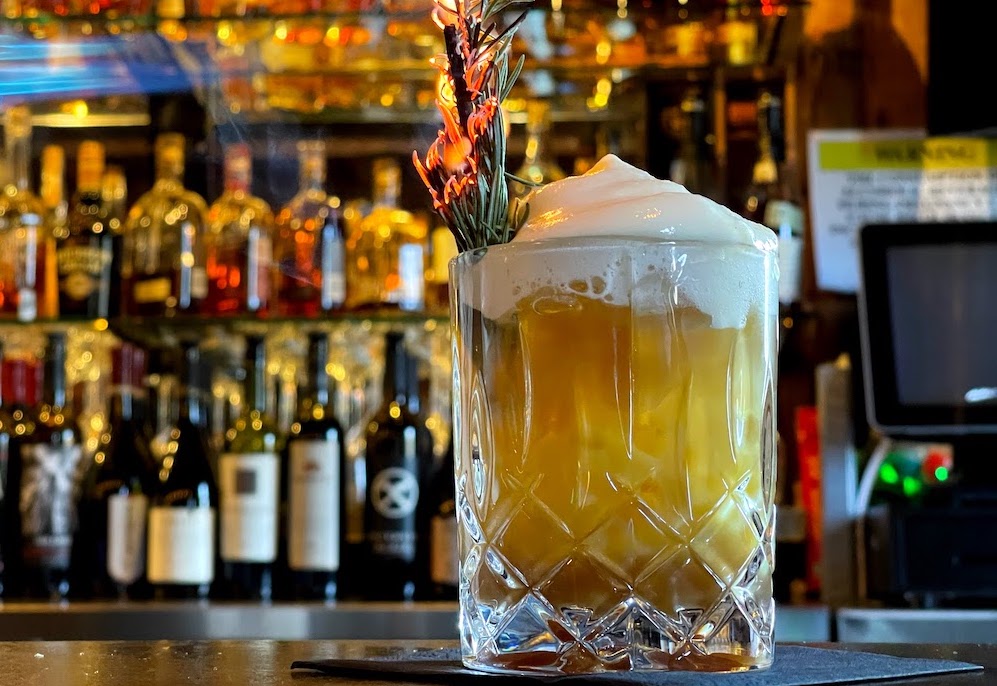 cocktail with rosemary spring sitting on a bar