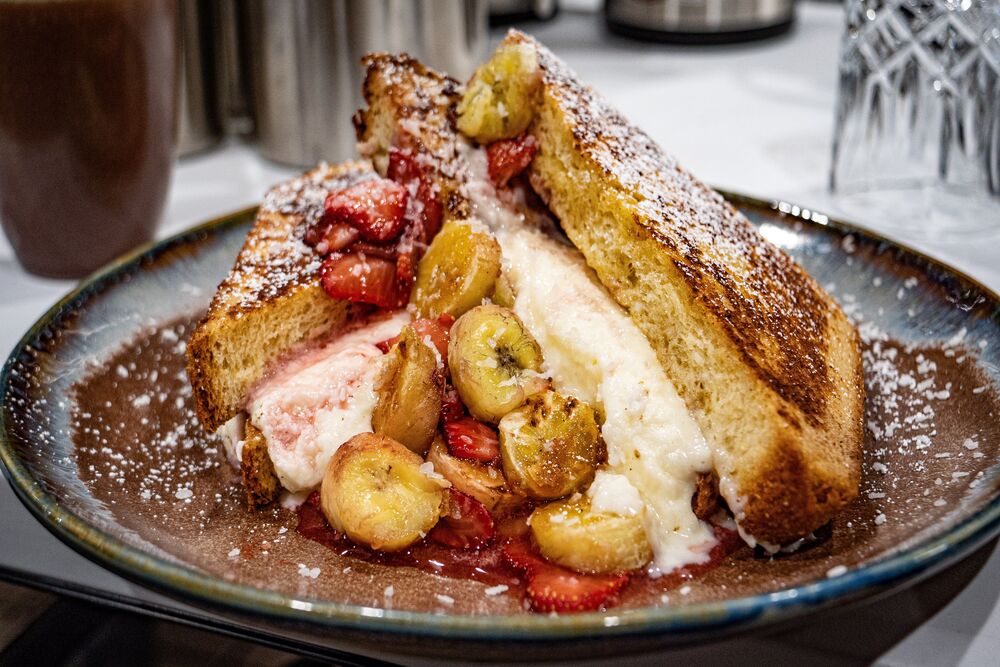 A brown and blue plate with the Stuffed French Toast with coconut cream filling, strawberry and bruleed banana topping